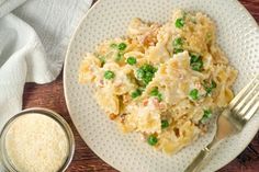 a white plate topped with pasta and peas next to a small bowl of seasoning