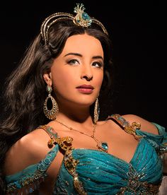 a woman wearing a tiara and jewelry in front of a black background with her hand on her hip