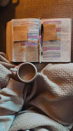 an open book on top of a bed next to a cup of coffee