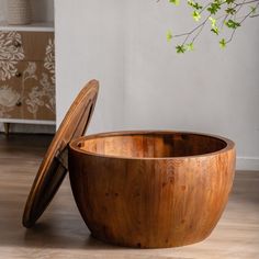 a large wooden bowl sitting on top of a hard wood floor next to a plant