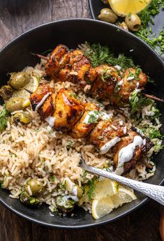 chicken skewers with rice and vegetables in a black bowl on a wooden table