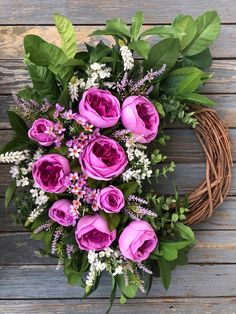 a wreath with purple flowers and greenery on a wooden surface, ready to be used as a decoration