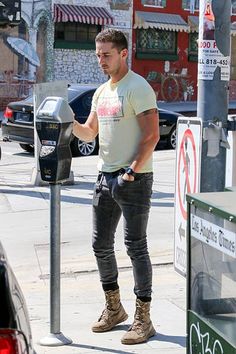 a man standing next to a parking meter on the side of a road with his hands in his pockets