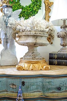 an ornate vase with white flowers on top of a dresser next to books and a wreath