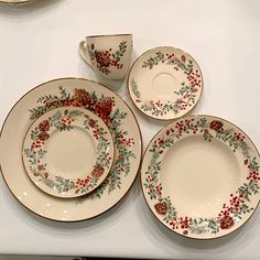 four plates and two cups with holly designs on them are sitting on a counter top