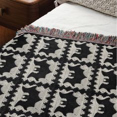 a black and white blanket on top of a bed next to a wooden dresser with drawers