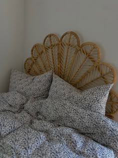 an unmade bed with blue and white floral bedspread, pillows and rattan headboard