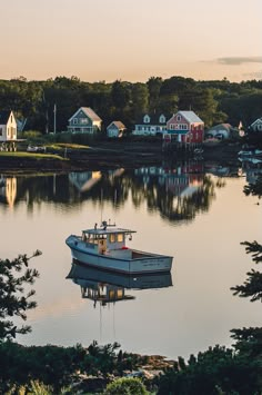 a small boat floating on top of a lake next to houses in the background at sunset