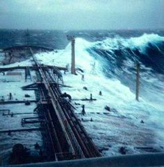 the ocean is full of large waves and people are standing on the pier in the water