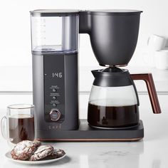 a coffee maker sitting on top of a counter next to a cup of coffee and cookies