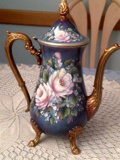 a blue teapot with flowers painted on it sitting on a doily next to a chair