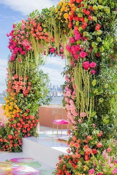 an arch covered in flowers and greenery next to the ocean