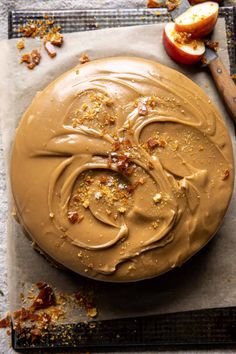 a cake with chocolate frosting and chopped nuts on top, next to an apple