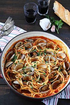 pasta with clams and parsley in a pan on a wooden table next to bread