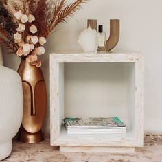 a vase with flowers next to a small white shelf on a marble countertop in front of a gold vase