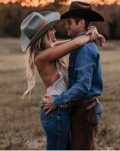 a man in a cowboy hat hugging a woman with his arms around her back while the sun is setting