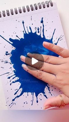 a woman's hand is touching a blue ink splatter on a notebook