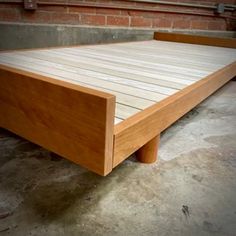 a wooden bed frame sitting on top of a cement floor next to a brick wall