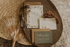 the wedding stationery is laid out on a wicker mat with a fan and tassel