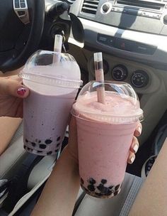 two people holding drinks in their hands while sitting in a car with steering wheel behind them