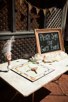 a sign that says please sign our guest board on the side of a table with feathers