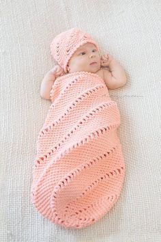 a baby wrapped in a pink crochet blanket laying on top of a bed