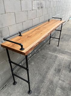 a wooden bench sitting on top of a sidewalk next to a brick wall and metal frame