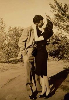 an old black and white photo of a man kissing a woman's forehead while standing on a dirt road