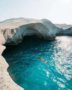 a person swimming in the water near an ice cave