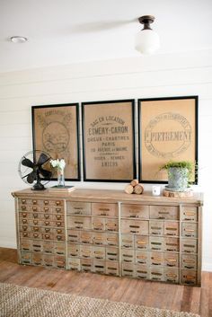 two framed pictures on the wall above an old filing cabinet with drawers in front of it