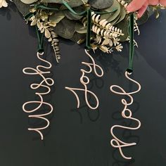 three metal letters are hanging on a black surface with greenery and leaves around them