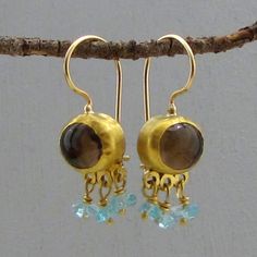 "With the oval Smoky Topaz, each earring is wonderfully balanced with 24k solid gold bezel and dangle green Apatite beads decorated each stone. For practicality and elegance, the hooks are handmade locking French wires made of 14k yellow gold with 9k gold backing. Earrings Width - 0.43'' ( 11 mm). Length without the ear wire - 0.7\" (18 mm). Length from top of the ear wire to bottom of the earring - 1.14\" (29 mm). The earrings will be packed in a gift box ready to be given as a gift, and will b Gold Drop Earrings With Blue Topaz, Gold Earrings With Gemstone Accents, Gold Teardrop Blue Topaz Earrings, Gold Oval Blue Topaz Earrings, Handmade Gold Earrings With Blue Topaz, Gold Briolette Fusion Earrings, Green Apatite, Smoky Topaz, Gold Dangle Earrings