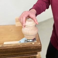 a person holding a piece of wood in their hand over a wooden object on top of a table