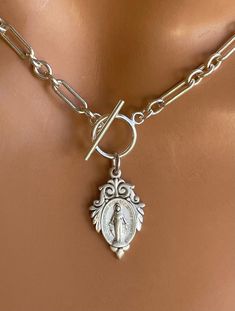 "This is a stunning thick, solid 925 sterling silver choker necklace with a unique Virgin Mary medallion that hangs from toggle clasp in front. This gorgeous Mother Mary charm measures 22x14mm and has the Miraculous Mary stamp with cross heart and stars on backside.. Made here is the USA by skilled silversmiths this pendant is absolutely incredible. This lovey sterling silver chunky chain links measure 8x4mm and 4mm, 3-1 pattern. Model is wearing a 15\" choker length. Comes in a gift box, ready Catholic Jewelry Necklace, 14kt Gold Jewelry, Sterling Silver Choker Necklace, Choker Necklace Gold, Clean Sterling Silver, Cross Heart, Sterling Silver Choker, Silver Choker Necklace, Catholic Jewelry