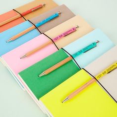 several different colored notebooks with pens on them