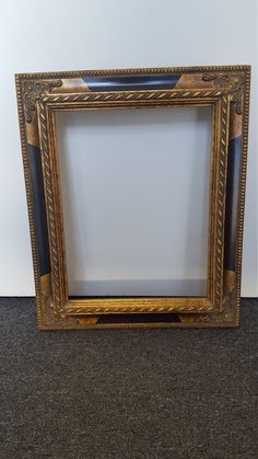 an ornate gold frame on the floor in front of a white wall with black carpet