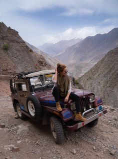 a woman sitting on top of a jeep in the mountains