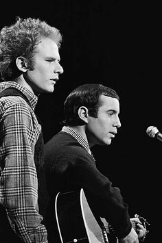 two men standing next to each other in front of a microphone and an acoustic guitar