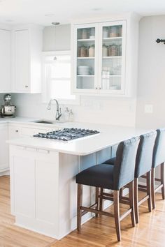 a kitchen with white cabinets and counter tops next to a stove top oven, sink and bar stools