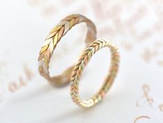 two gold wedding rings on top of each other with leaves in the middle, sitting on a white surface