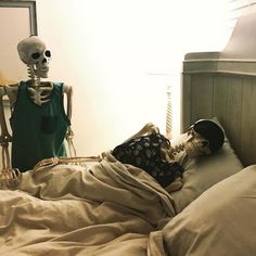 there is a skeleton laying in bed with a human head on the pillow next to him