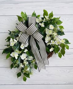 a wreath with white flowers and green leaves on a wooden background, tied with a ribbon