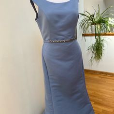 a blue dress on display in front of a wall and potted plant next to it