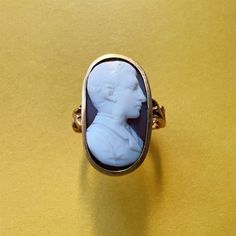 For sale a 18th Century 18K gold empire period cameo ring. This rare ring showcases a remarkable white and brown two-colored hard stone cameo portraying the profile of a distinguished gentleman. The intricacies of his hair, beard, and clothing are nothing short of astonishing, each detail meticulously crafted to perfection. The oversized cameo, measuring an impressive 2,2cm by 1,2cm, transforms this ring into a captivating statement piece when adorned. The sheer size of the cameo ensures that it commands attention, making it the perfect accessory for those who appreciate the grandeur of antique jewelry. The shoulders of the ring are equally enchanting, adorned with sensational floral motifs resembling two delicately intertwined branches of leaves. These intricate details add a touch of rom Vintage Carved Signet Ring For Formal Occasions, Elegant Formal Signet Ring With Intaglio, Formal Oval Engraved Ring With Intaglio, Oval Engraved Ring With Intaglio For Formal Events, Formal Oval Rings With Historical Design, Formal Oval Ring With Historical Design, Elegant Oval Intaglio Signet Ring, Formal Oval Signet Ring With Intaglio, Oval Intaglio Signet Ring For Formal Occasions