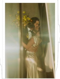 a man and woman standing next to each other in front of a mirror with flowers on it