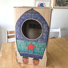 a cardboard box with a rocket ship design on the front and sides, sitting on a wooden table