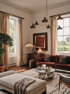 a living room filled with lots of furniture next to two large windows covered in curtains