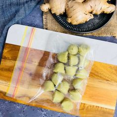 some food is wrapped in plastic on top of a cutting board and next to a bowl of ginger