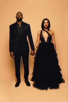 a man and woman standing next to each other in formal wear, one wearing a black dress