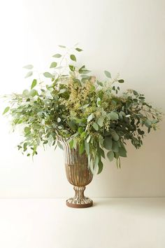 a vase filled with lots of greenery on top of a table